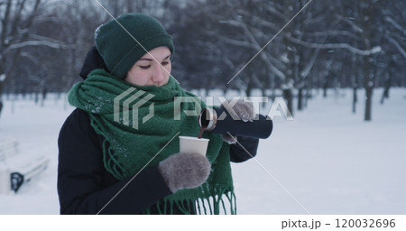 teenage girl pouring hot cocoa into paper cup in park on a winter day teenage girl pouring hot cocoa into paper cup in park on a winter day 120032696