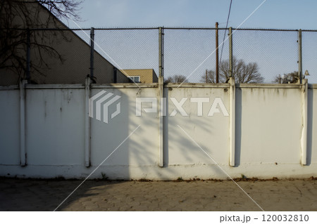 White wall with chain-link fence and shadows in an urban environment 120032810