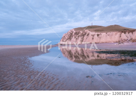 Experience the serene beauty of coastal cliffs reflected on a tranquil beach landscape at sunset 120032917