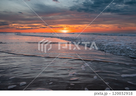 Tranquil beach evening with vibrant sunset colors over ocean waves, creating serene landscape Tranquil beach evening with vibrant sunset colors over ocean waves, creating serene landscape 120032918