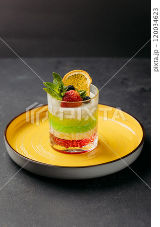 Colorful layered dessert in a glass, topped with fresh fruits and mint, served on a vibrant plate 120034623