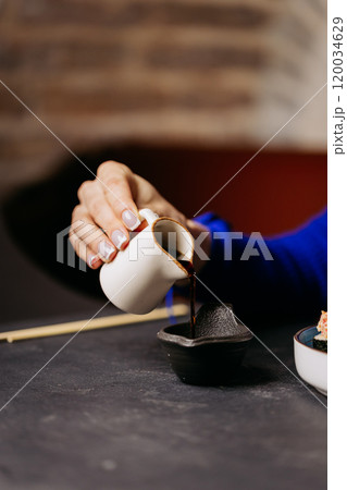Close-up of a hand pouring soy sauce into a dipping bowl, perfect for sushi or Japanese cuisin Close-up of a hand pouring soy sauce into a dipping bowl, perfect for sushi or Japanese cuisin 120034629