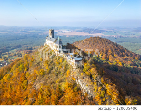 The stunning Bezdez medieval castle is showcased from above, surrounded by vibrant autumn foliage. The landscape features rolling hills and rich colors typical of the season. 120035400