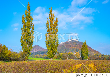 The stunning Bezdez Castle rises majestically on a hill, surrounded by vibrant autumn foliage, under a clear blue sky, showcasing the beauty of the Czech landscape during fall. 120035404