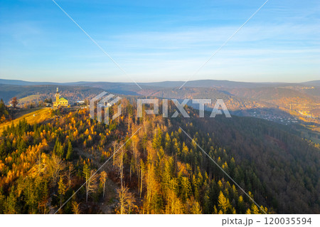 As the sun sets over the Jizera Mountains, the Tanvaldsky Spicak lookout tower stands tall amidst vibrant autumn foliage, offering breathtaking views of the surrounding hills and valleys. 120035594