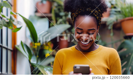A joyful woman in a yellow sweater smiles while using her smartphone in a lush indoor garden setting A joyful woman in a yellow sweater smiles while using her smartphone in a lush indoor garden setting 120035660