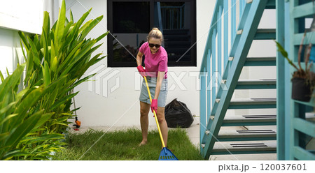 A woman raking the lawn at the backyard of her house A woman raking the lawn at the backyard of her house 120037601