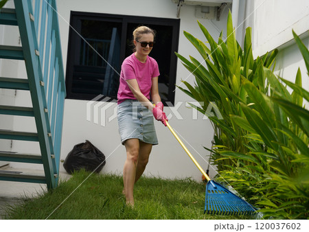 A woman raking the lawn at the backyard of her house A woman raking the lawn at the backyard of her house 120037602