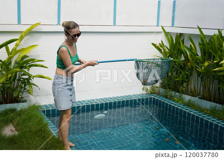 A young woman clean leaves out of a pool  120037780
