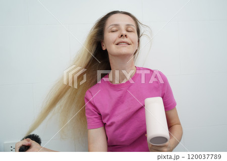 A woman is expertly styling her hair using a blow dryer and brush while in the bathroom 120037789