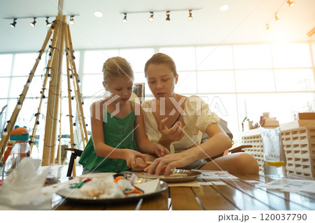 Mother and her daughter paint Halloween cookies  120037790