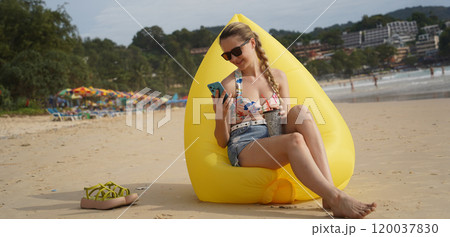 A young woman on the beach lounging on a yellow bean bag  120037830