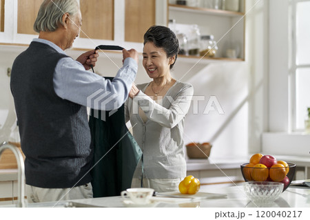 senior asian man helping wife putting on apron senior asian man helping wife putting on apron 120040217