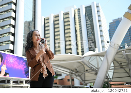 Cheerful mature businesswoman enjoying a phone conversation in front of skyscrapers 120042721