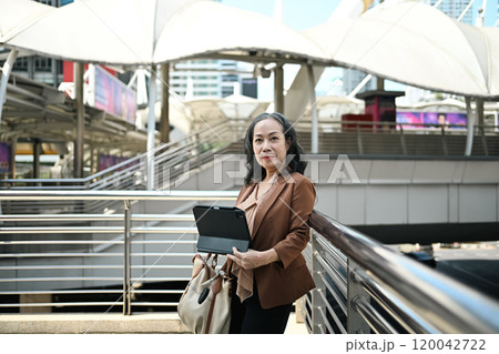 confident mature entrepreneur holding digital tablet standing in urban area confident mature entrepreneur holding digital tablet standing in urban area 120042722