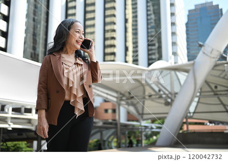 Mature businesswoman having a phone conversation in a modern cityscape 120042732