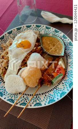 A plate of authentic traditional local Indonesian meal of nasi goreng or fried rice and satay skewers served with saus kacang or peanut sauce  120044421