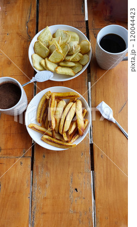 Rustic wooden table setting with mugs of coffee, bowls of pritong saging or fried banana and sweet potatoes or kamote for a traditional Filipino afternoon snack Rustic wooden table setting with mugs of coffee, bowls of pritong saging or fried banana and sweet potatoes or kamote for a traditional Filipino afternoon snack 120044423