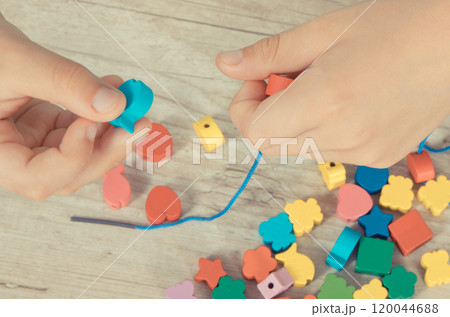 Preschooler making bracelet from thread and wooden colored beads 120044688