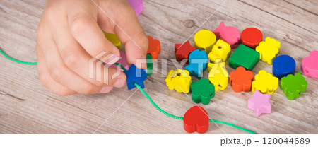 Preschooler making bracelet from thread and wooden colored beads Preschooler making bracelet from thread and wooden colored beads 120044689