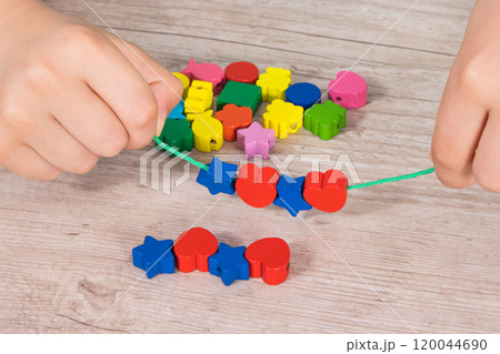 Preschooler making bracelet from thread and wooden colored beads 120044690