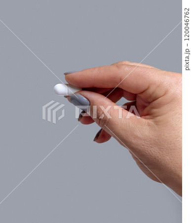Female hand holding a white pill with fingers closeup against grey, Healthcare concept 120046762