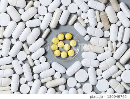 White medical capsules and pills with yellow pills in the middle on grey top view 120046763