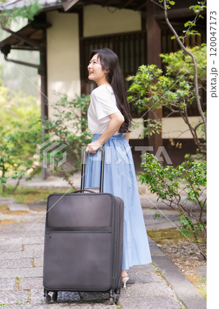 キャリーケースを引いて田舎に帰省する若い女性　旅行イメージ  120047173