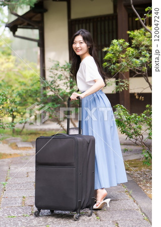 キャリーケースを引いて田舎に帰省する若い女性　旅行イメージ  120047240