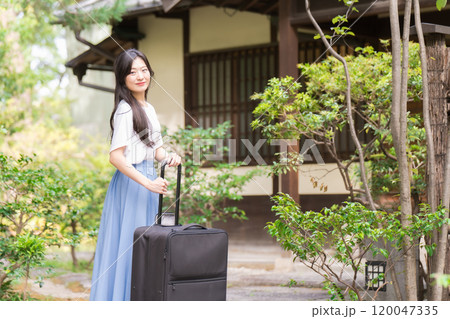 キャリーケースを引いて田舎に帰省する若い女性　旅行イメージ  120047335