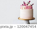 A pastel pink cream cake with buttercream flowers decoration and gold sprinkles with real flowers on a cake stand. 120047454