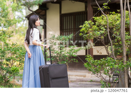 キャリーケースを引いて田舎に帰省する若い女性　旅行イメージ  120047761