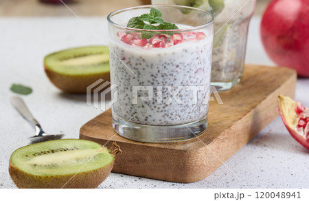 Two glasses of chia yogurt dessert garnished with fresh fruit, pomegranate seeds and kiwi slices 120048941