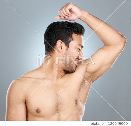 Health, fresh and man smelling armpit in studio for hygiene, clean and wellness routine. Wellness, fragrance and male person checking underarm scent for deodorant or perfume by gray background. 120049000