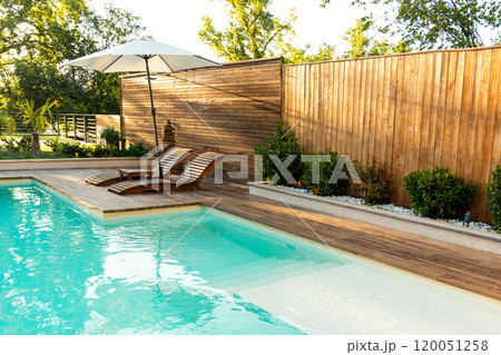Swimming pool in modern private villa with lounge chairs, palm trees and umbrella 120051258