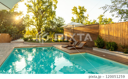 Swimming pool in modern private villa with lounge chairs, palm trees and umbrella at sunset 120051259
