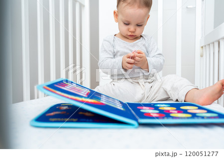 Little baby girl playing with busy book while sitting in crib. Concept of quiet books and modern educational toys 120051277