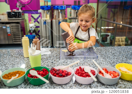 Little girl learning how to cook in a cooking class. Handmade dessert. Making chocolate candy, Child filling heart shaped mold with chocolate 120051838