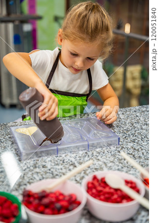 Little girl learning how to cook in a cooking class. Handmade dessert. Making chocolate candy, Child filling heart shaped mold with chocolate 120051840