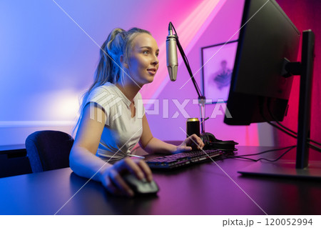 Smiling and focused professional gamer girl with headset play online multiplayer video game on PC 120052994
