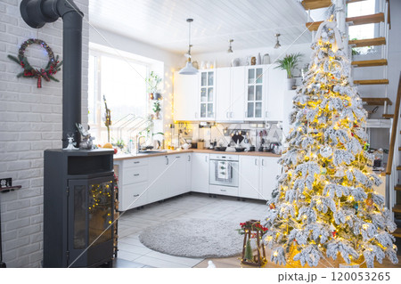 Festive white modern interior of house is decorated for Christmas and New Year in loft style with black stove, fireplace, Christmas tree. Potted plants, firewood in the woodpile 120053265