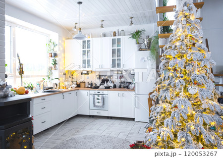 Festive Christmas decor in white kitchen, modern village interior with a snowy Christmas tree and fairy lights. New Year, Christmas mood, cozy home, Metal modular staircase. The general plan Festive Christmas decor in white kitchen, modern village interior with a snowy Christmas tree and fairy lights. New Year, Christmas mood, cozy home, Metal modular staircase. The general plan 120053267