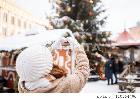 Young woman holding hands in the shape of a heart against the background of a Christmas tree. Young woman holding hands in the shape of a heart against the background of a Christmas tree. 120054406