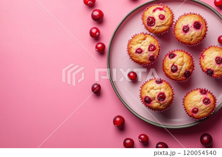 Freshly baked cranberry muffins arranged on a glass plate with scattered cranberries against a pink 120054540