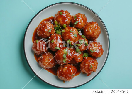 Delicious homemade meatballs coated in a rich sauce, garnished with green onions on a bright blue Delicious homemade meatballs coated in a rich sauce, garnished with green onions on a bright blue 120054567