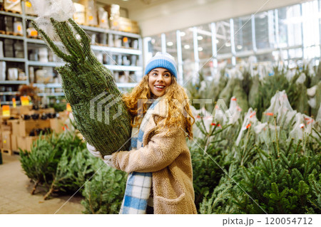 young smiling woman chooses Christmas tree to buy. Happy woman buying New Year tree for Christmas. young smiling woman chooses Christmas tree to buy. Happy woman buying New Year tree for Christmas. 120054712