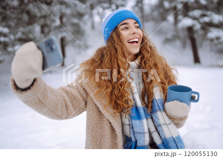 Portrait of a beautiful woman in warm clothes takes selfie with a hot drink from a thermos in hands. Portrait of a beautiful woman in warm clothes takes selfie with a hot drink from a thermos in hands. 120055130