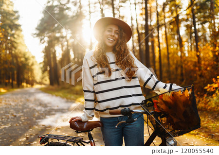 Smilling woman with bicycle enjoying autumn weather in park. Woman walking in autumn forest. Smilling woman with bicycle enjoying autumn weather in park. Woman walking in autumn forest. 120055540