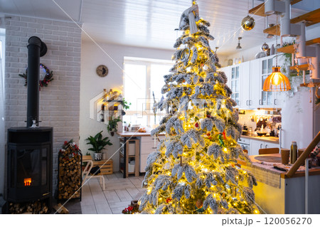 Festive white modern interior of house is decorated for Christmas and New Year in loft style with black stove, fireplace, Christmas tree. Potted plants, firewood in the woodpile Festive white modern interior of house is decorated for Christmas and New Year in loft style with black stove, fireplace, Christmas tree. Potted plants, firewood in the woodpile 120056270