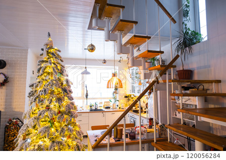 Christmas decor in white kitchen, modern village interior with a snowy Christmas tree and fairy lights. New Year, Christmas mood, cozy home, Metal modular staircase. 120056284